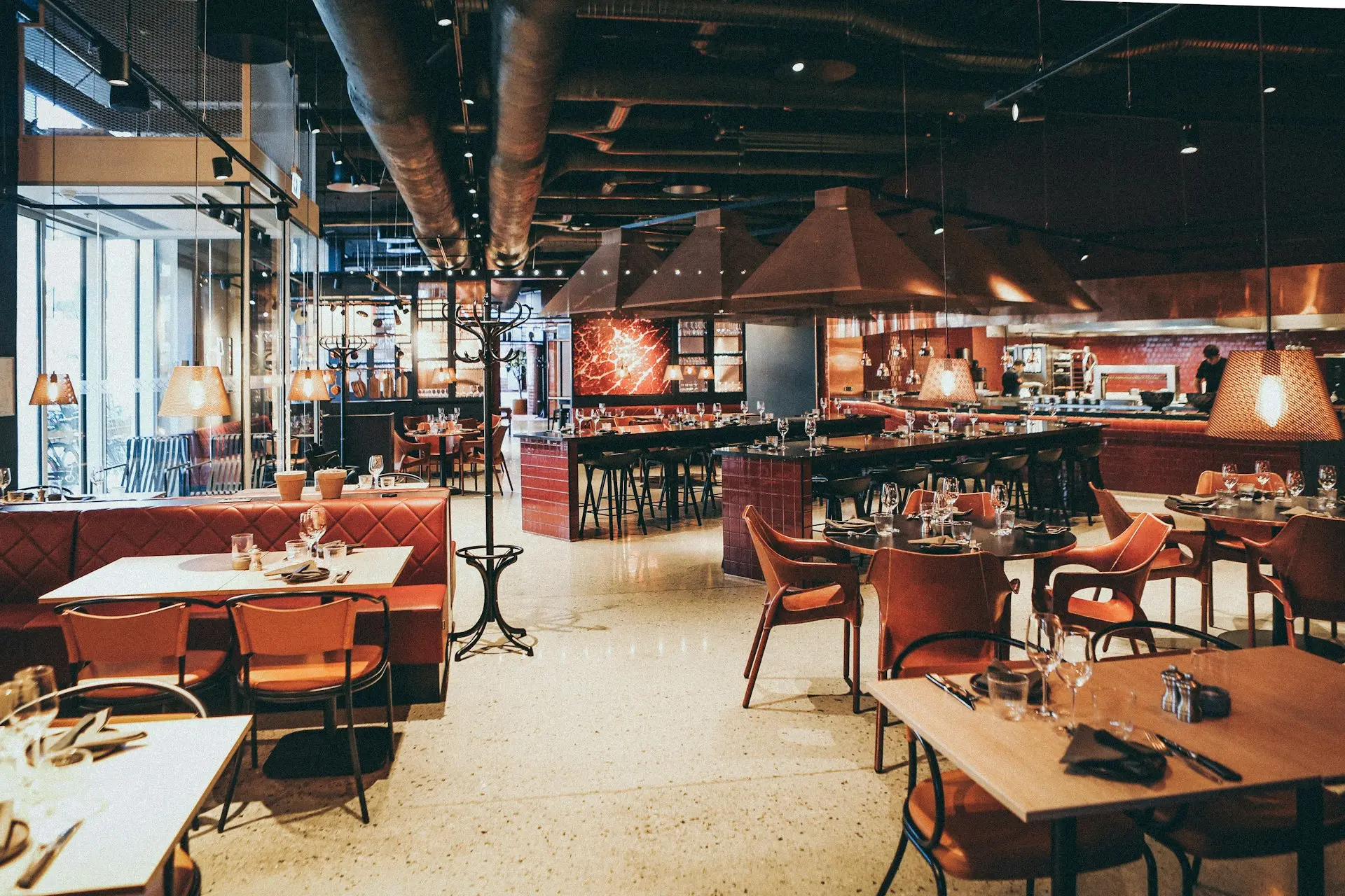 A modern restaurant interior with red leather booths, wooden tables, and hanging pendant lights